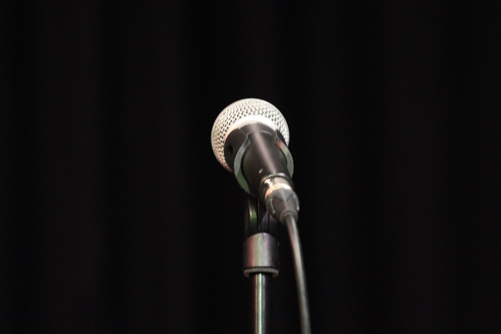 Silver stage microphone on a black stand in front of a dark curtain