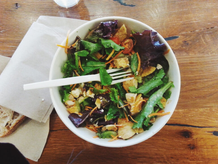 Bowl of fresh leafy salad with a fork on a wooden table