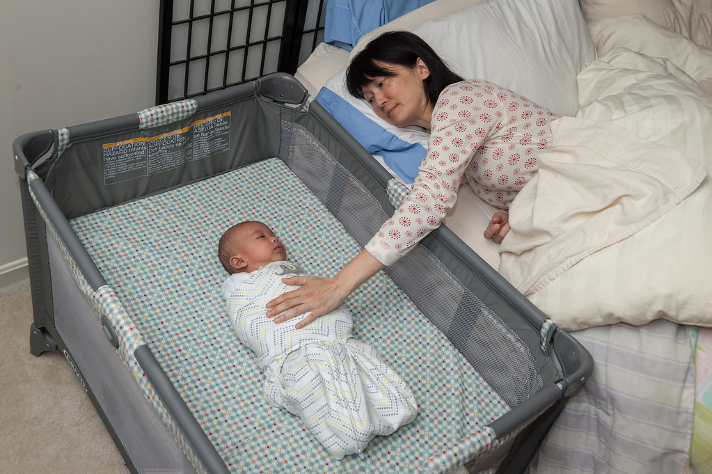 Mother lying in bed and gently touching her baby sleeping in a nearby bassinet