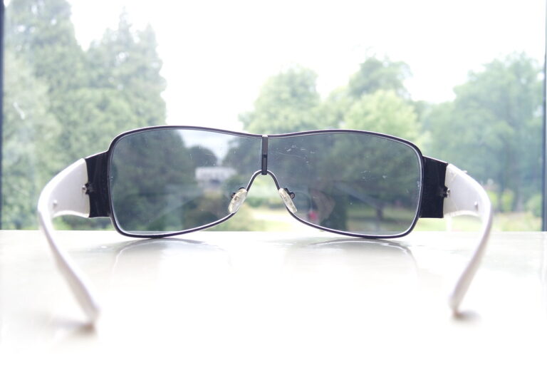 Pair of sunglasses resting on a white table in front of a window with trees