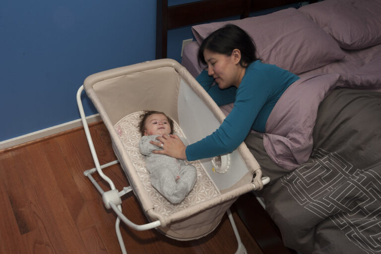 Mother leaning from her bed to gently touch her baby lying in a bassinet