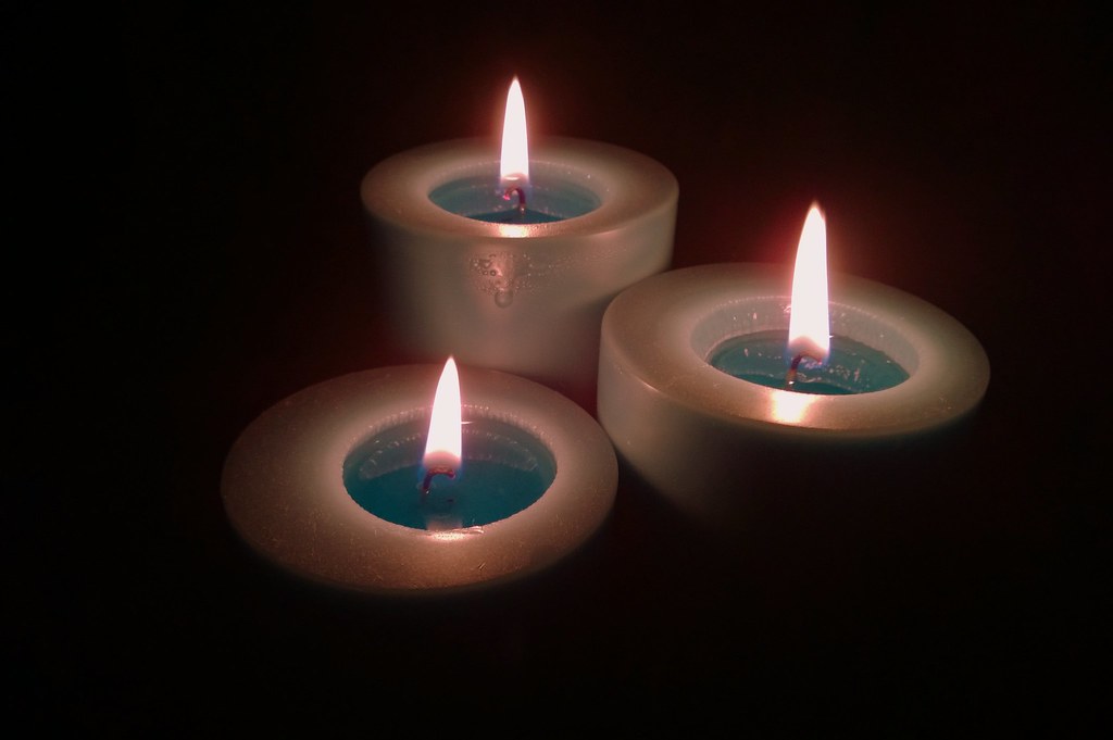 Three lit candles glowing softly in a dark room for a calm evening