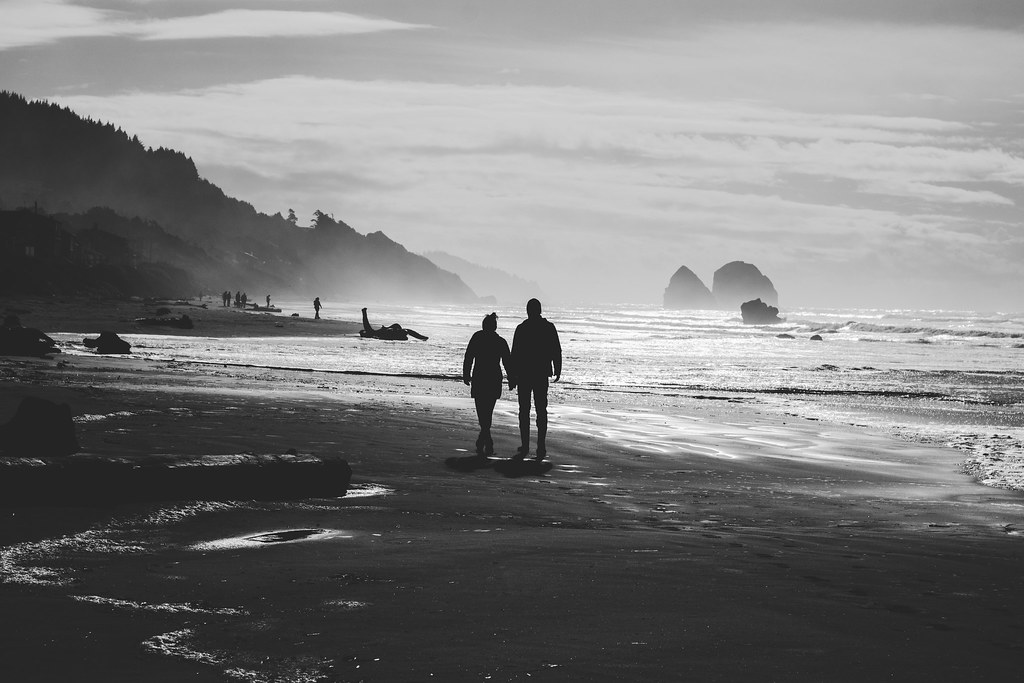 Couple holding hands while walking together along a misty ocean beach