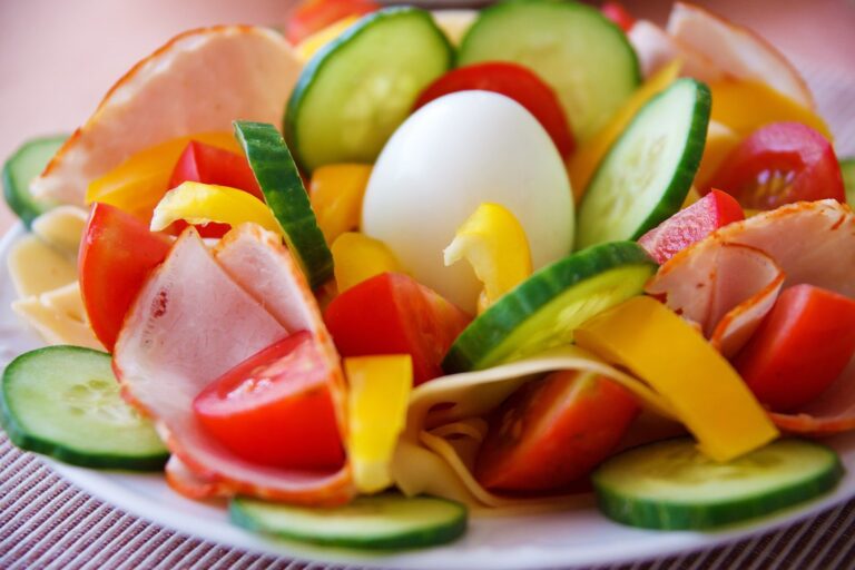 Colorful plate of sliced cucumber, tomatoes, yellow pepper, ham and a boiled egg