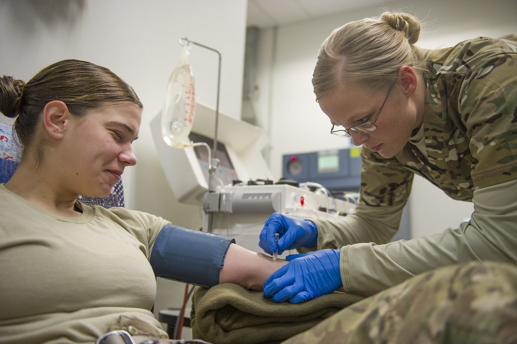 Health worker in blue gloves drawing a blood sample from a woman's arm in a clinic