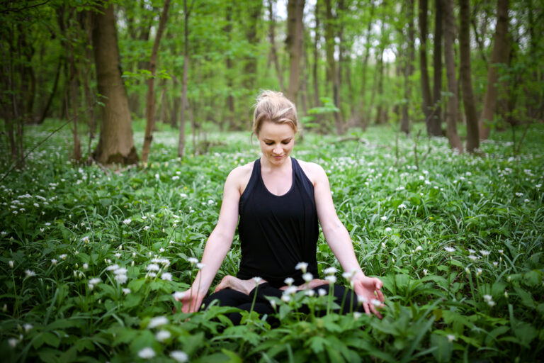 Woman sitting cross-legged and breathing calmly among green plants in a forest