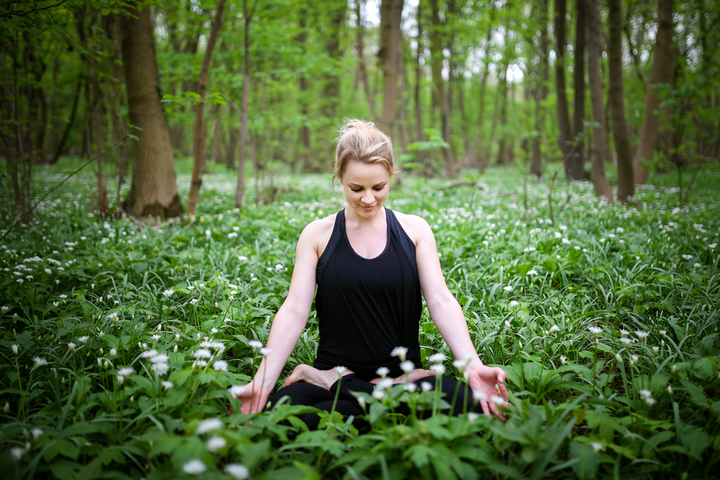Woman sitting cross-legged and breathing calmly among green plants in a forest