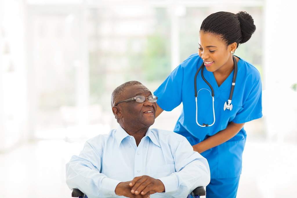 Smiling nurse in blue scrubs caring for an older man in a bright clinic