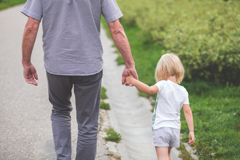 An older man walking hand in hand with a young girl along a garden path