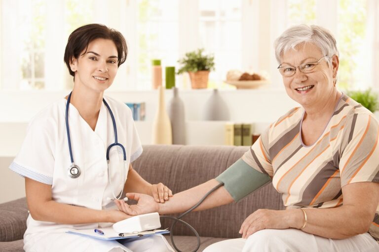 Friendly doctor checking the blood pressure of a smiling older woman at home