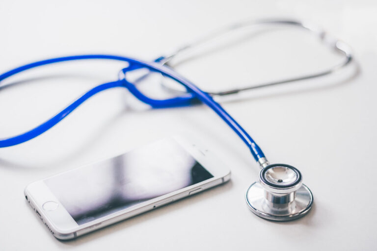 Blue stethoscope lying next to a smartphone on a clean white table