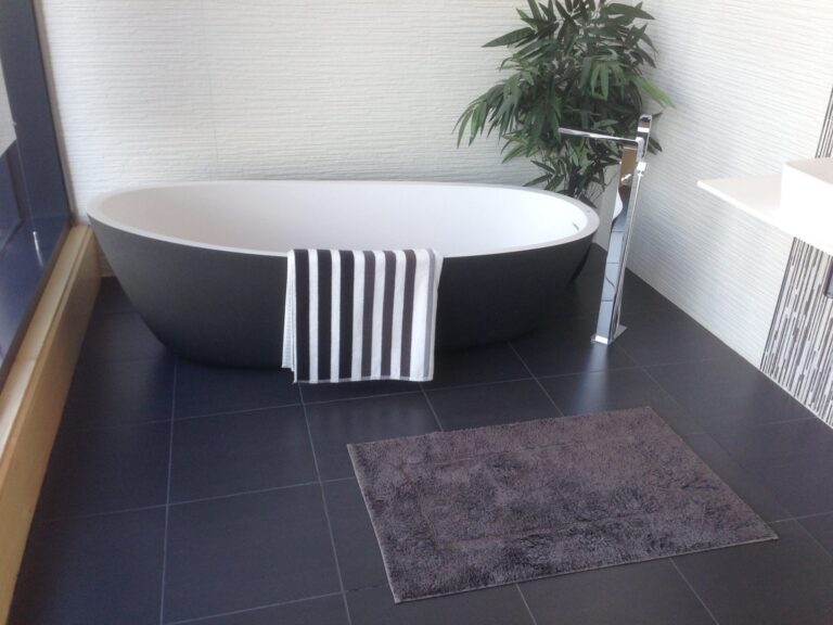 Modern bathroom with a dark bathtub, striped towel, grey bath mat and green plant