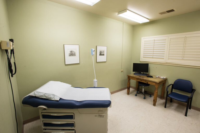 Clean, quiet clinic examination room with a padded exam table and chair