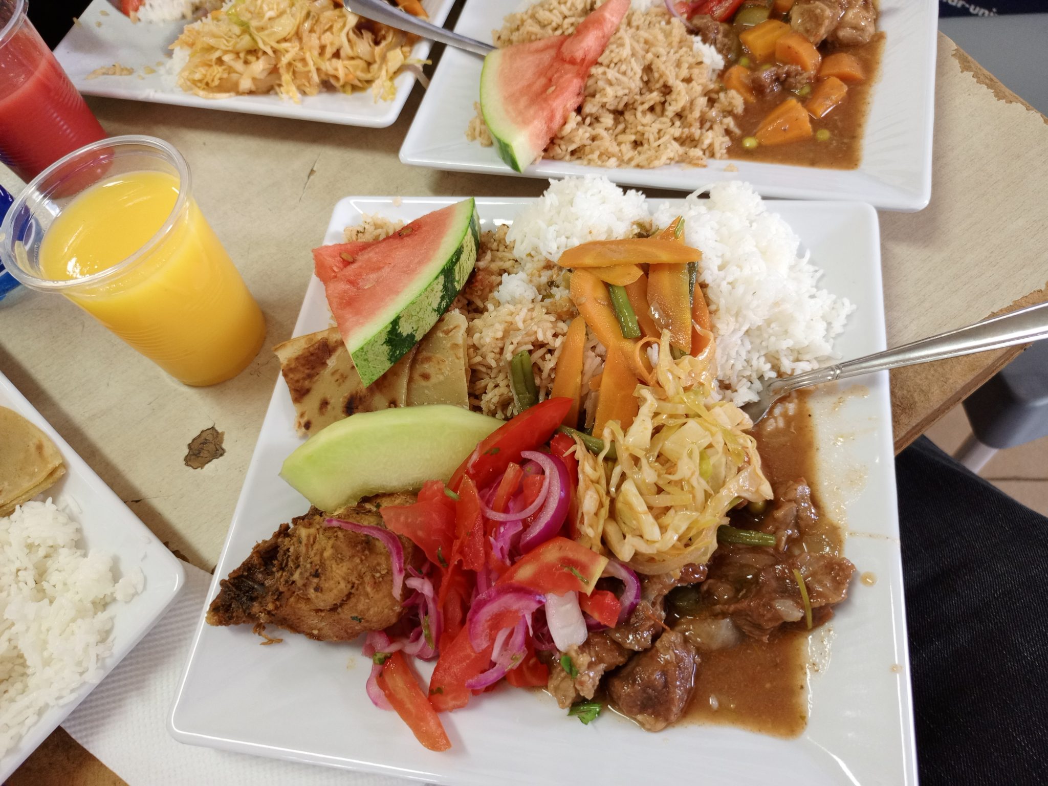 Plate of rice, stewed meat, fresh tomato salad, carrots and watermelon slices on a table