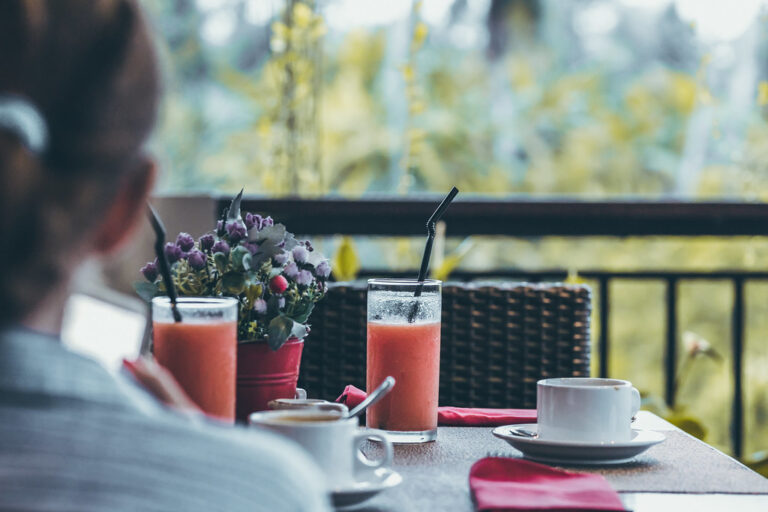 Woman having a calm morning breakfast with fresh juice and coffee on a green terrace