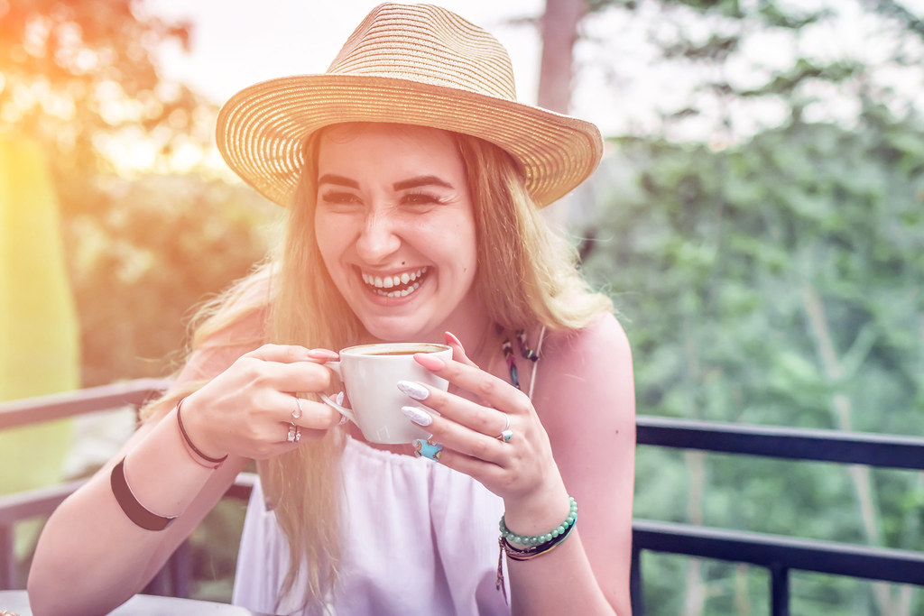 Smiling woman in a straw hat enjoying a cup of tea on a balcony