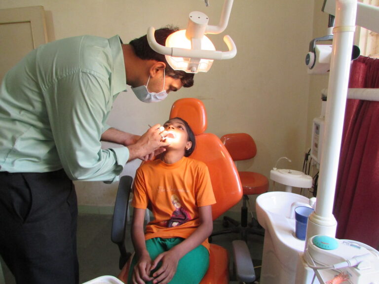 Dentist in a mask examining a young boy's teeth in an orange dental chair