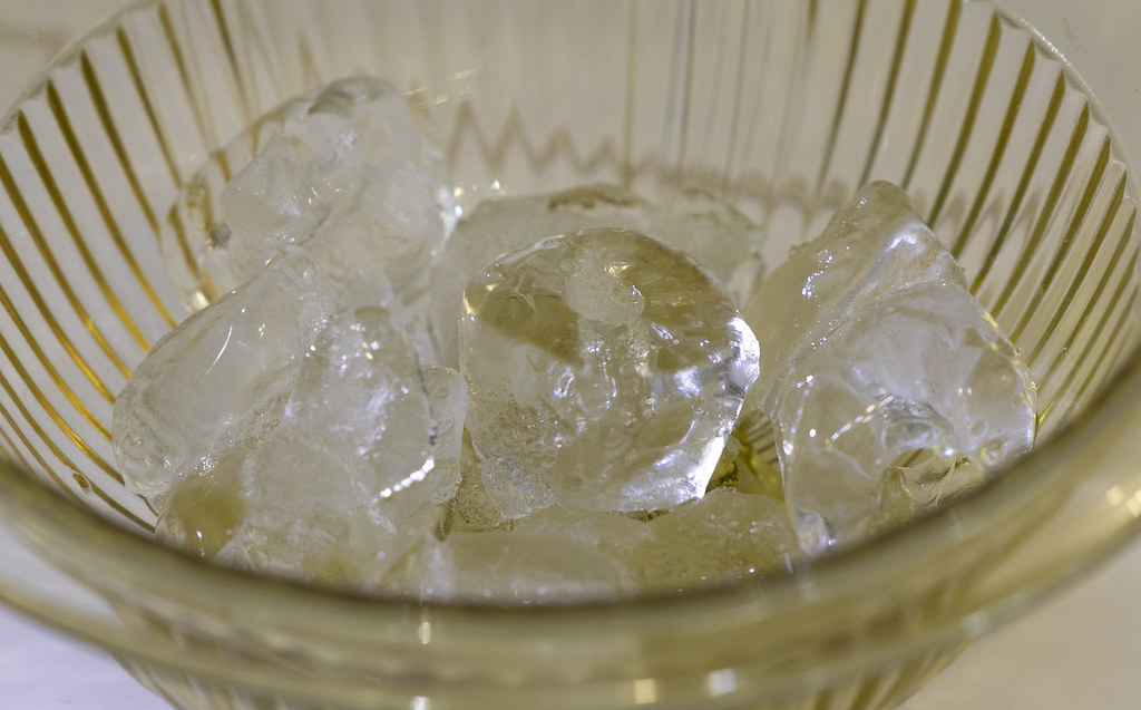 Clear ice cubes piled inside a ribbed glass bowl on a light table