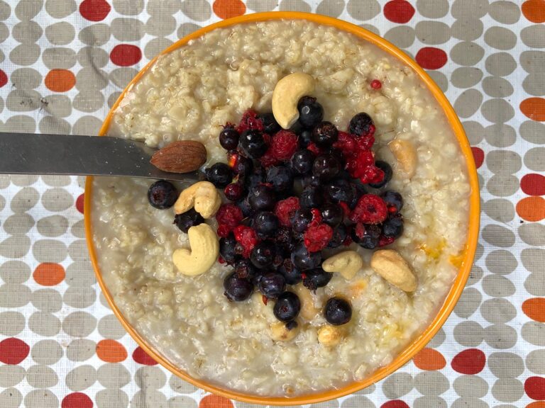 Bowl of oatmeal topped with blueberries, raspberries and cashew nuts on a spotted cloth