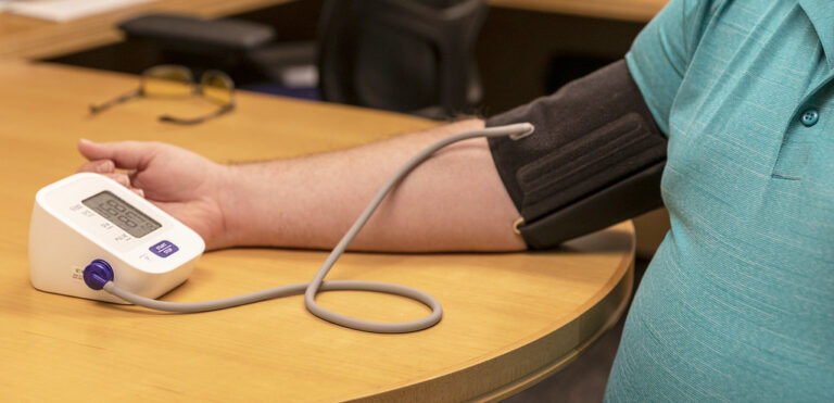 Person resting an arm on a table while a digital blood pressure cuff takes a reading
