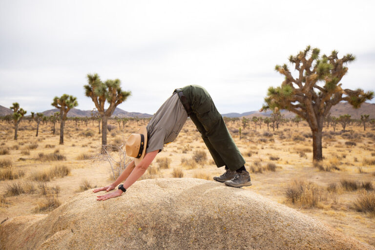Park ranger in a hat doing a downward dog stretch on a desert rock