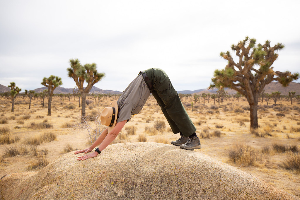 Park ranger in a hat doing a downward dog stretch on a desert rock