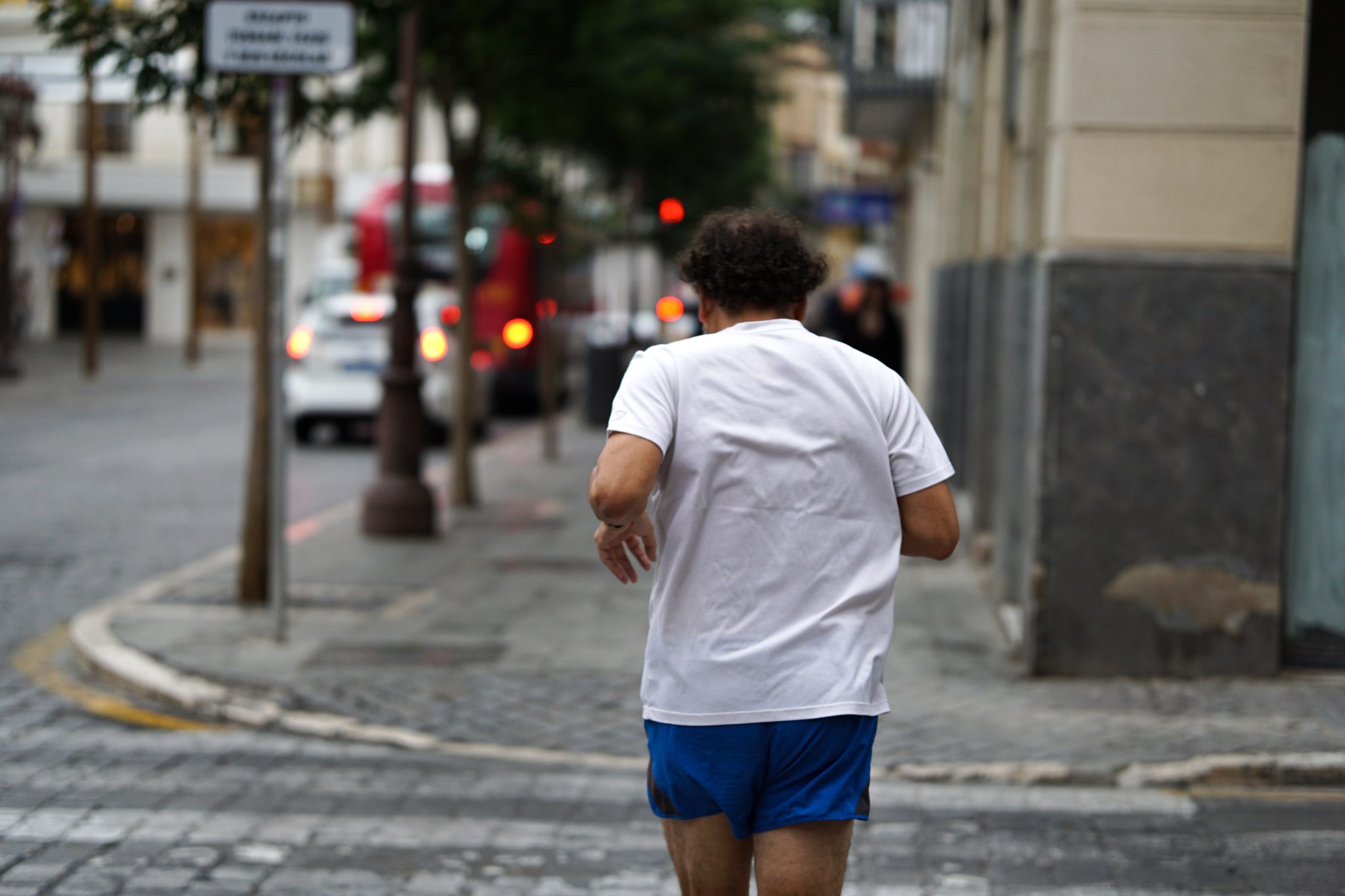 Man in a white t-shirt and blue shorts jogging along a quiet city street
