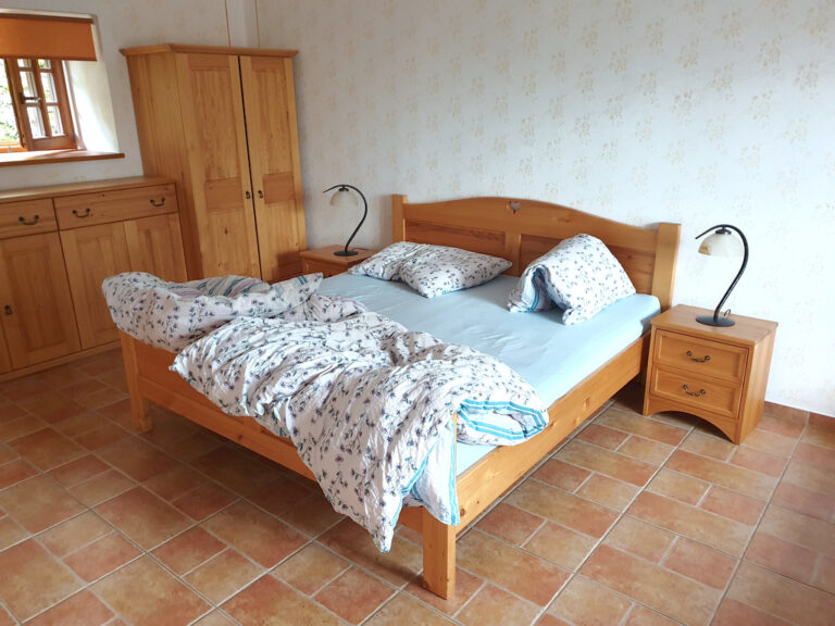 Simple wooden bed with soft bedding and matching bedside lamps in a tidy bedroom