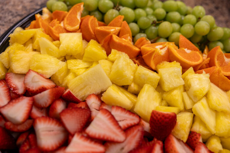 Colourful fruit platter with sliced strawberries, pineapple chunks, orange wedges and green grapes