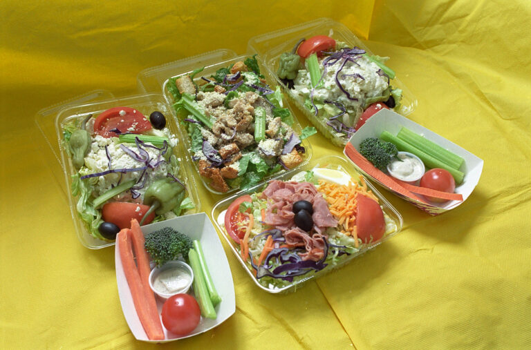 Colourful fresh salads with tomatoes, greens and vegetables in trays on a yellow table