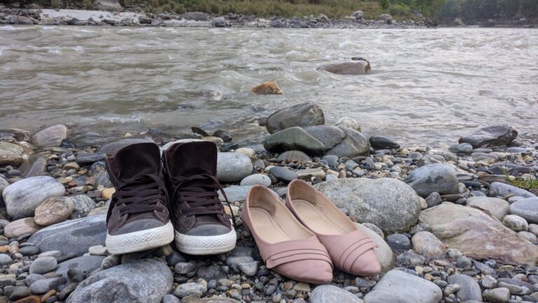 A pair of brown sneakers and pink flat shoes on river stones by flowing water