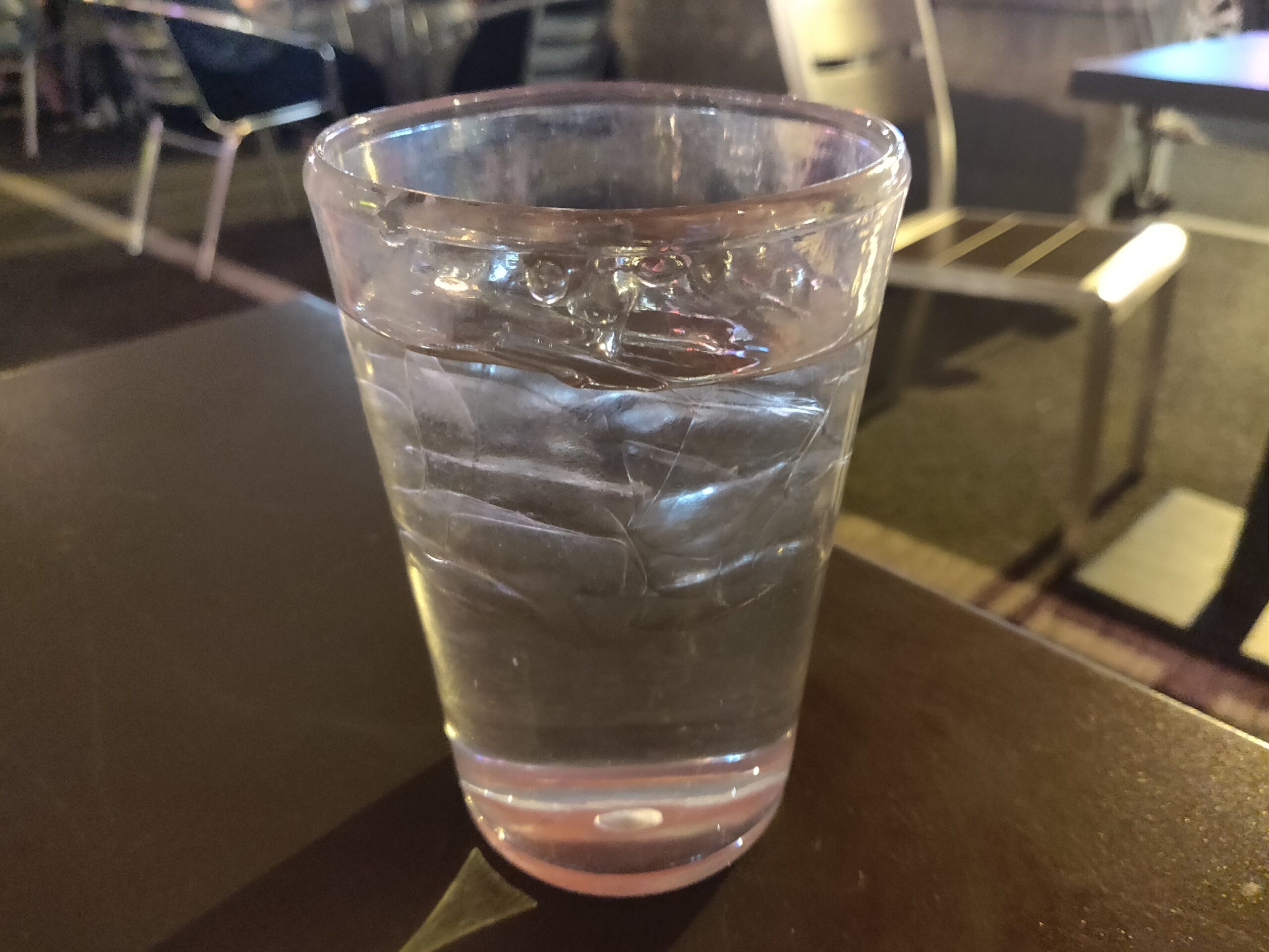 Clear glass of cold water with ice cubes sitting on a dark cafe table