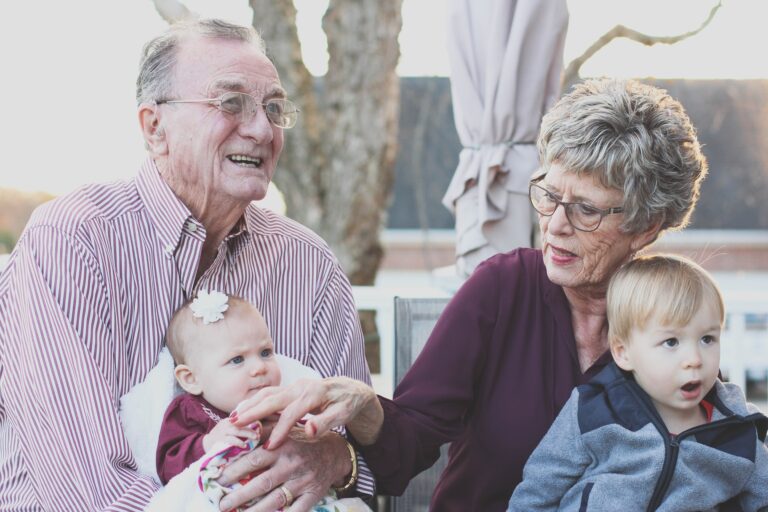 Smiling grandparents sitting outdoors while holding their baby granddaughter and young grandson