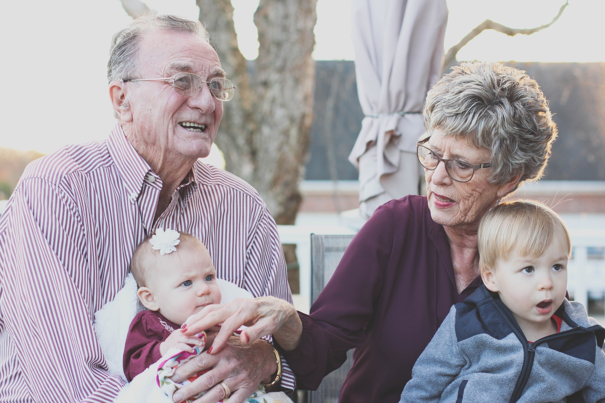 Smiling grandparents sitting outdoors while holding their baby granddaughter and young grandson