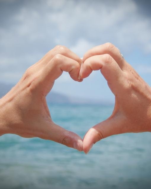 Two hands forming a heart shape against a blue sea and sky