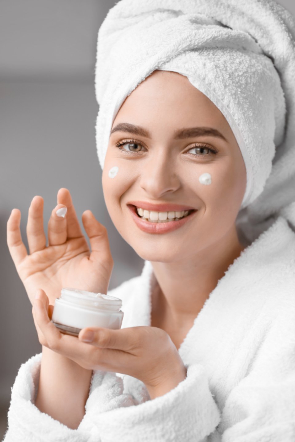 Smiling woman in a white towel holding a jar of face cream