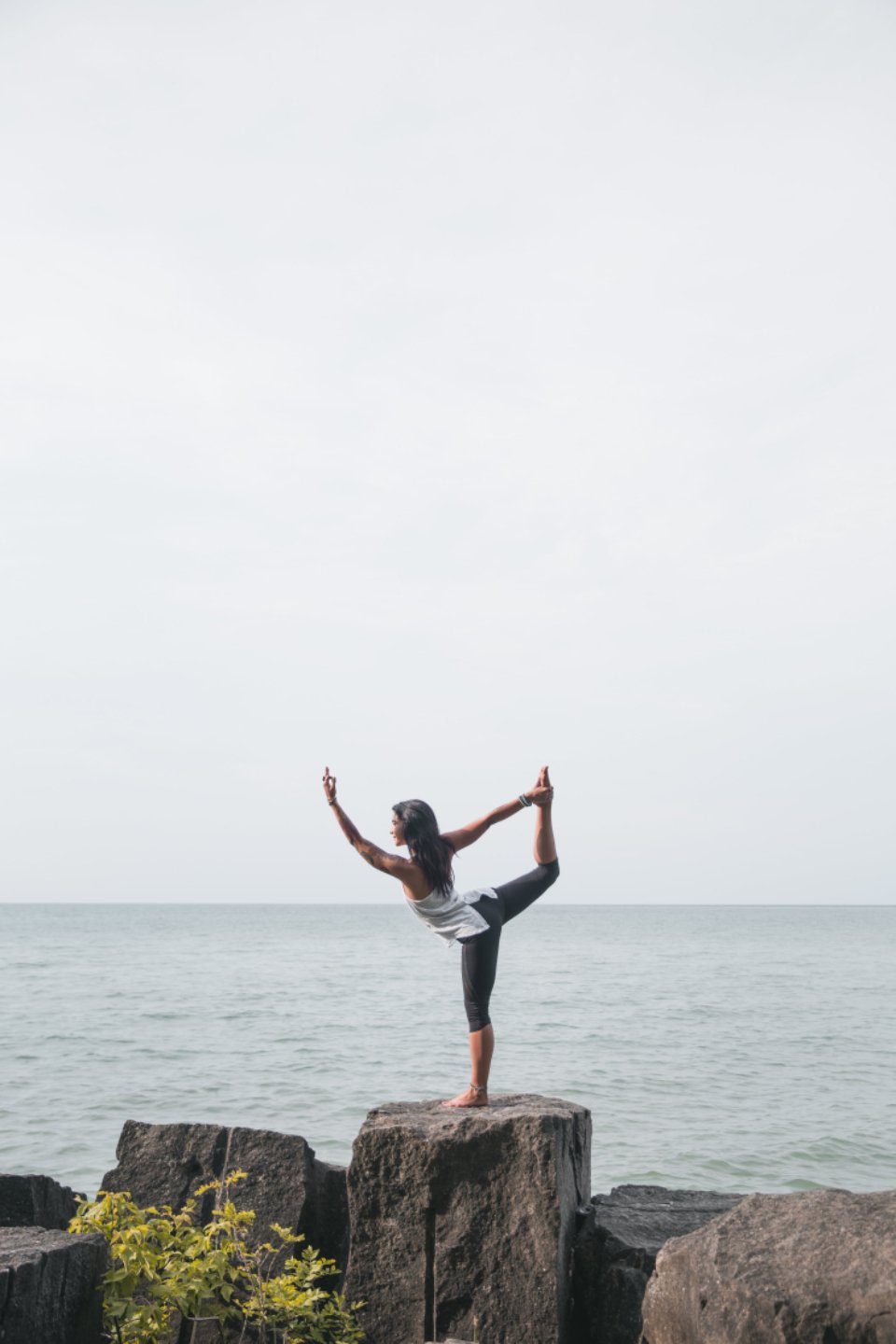 Woman doing a balancing yoga pose on a rock beside calm water