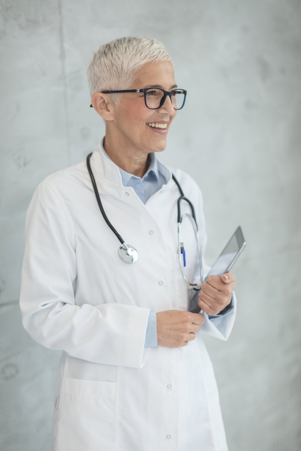 Smiling female doctor in a white coat holding a tablet in a bright clinic